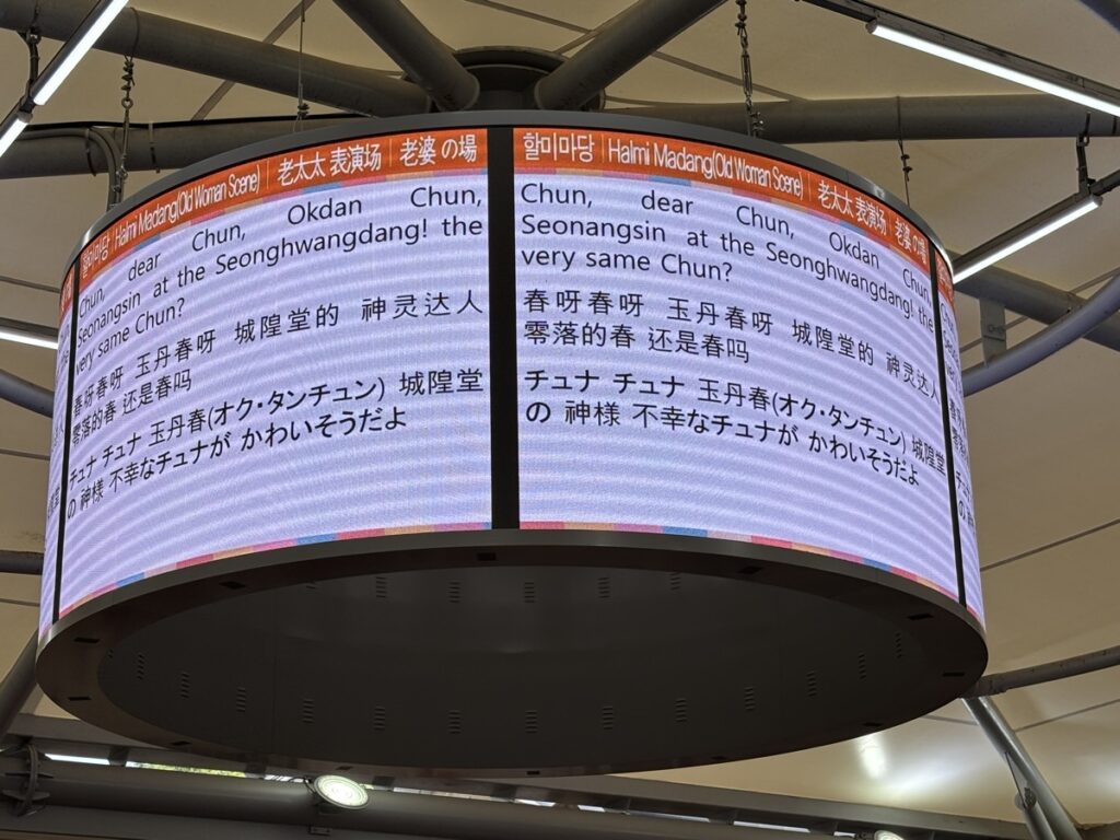 ３ヶ国語の字幕が表示された舞台上部のモニターの写真